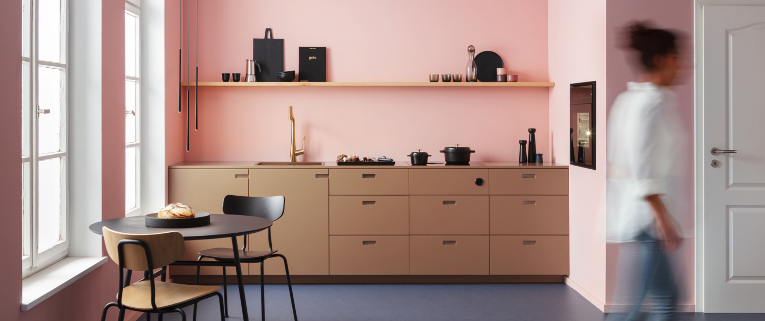 Bilde av et lite, moderne rosa kjøkken og en dame som er uskarp - illustrerer BORA S Pure er laget til de minste kjøkken og gir overraskende mange muligheter.
